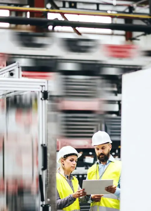 Zwei Arbeiter stehen mit Warnwesten vor einer industriellen Anlage
